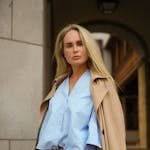 Fashionable woman wearing trench coat and denim stands in a city street.